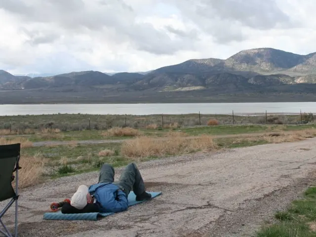 Barry resting on a blanket beside the road, with mountains and a lake behind him